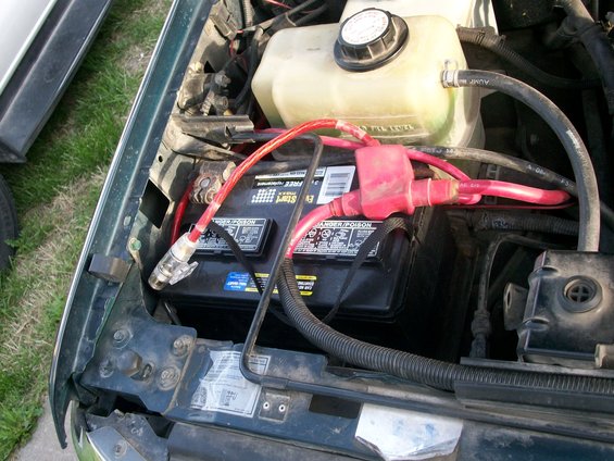 Engine bay showing battery, red cables, and coolant reservoir