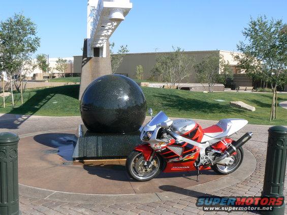 Red and silver Honda motorcycle parked next to a large black sphere sculpture