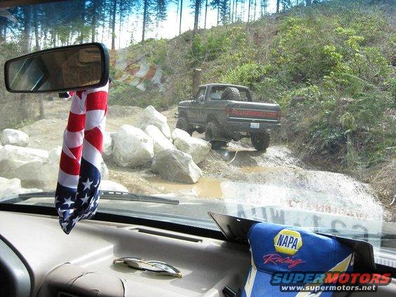 Dark pickup truck with spare tire on back, seen from interior, driving off-road