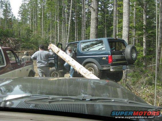 1992 Ford Bronco with a log being moved by people in a forest, another truck visible
