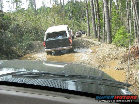1992 Ford Bronco driving through mud on a forest road
