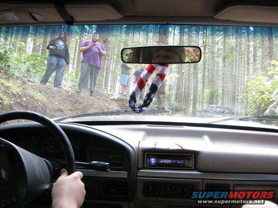 Interior view from driver's seat of a vehicle on a forest road; people stand on the embankment. Another vehicle is visible in the distance