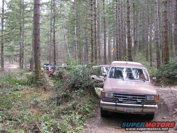 Brown Ford Econoline van on dirt road, front view. Baja lights on bumper
