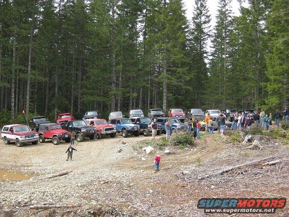 Group of off-road vehicles parked in a wooded area with people gathered around