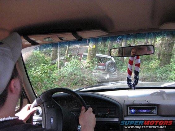 View from inside a vehicle driving on a trail, with another off-road vehicle ahead in the trees