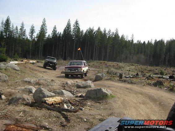 Maroon and white SUV with orange flag on a dirt trail, another dark SUV behind it