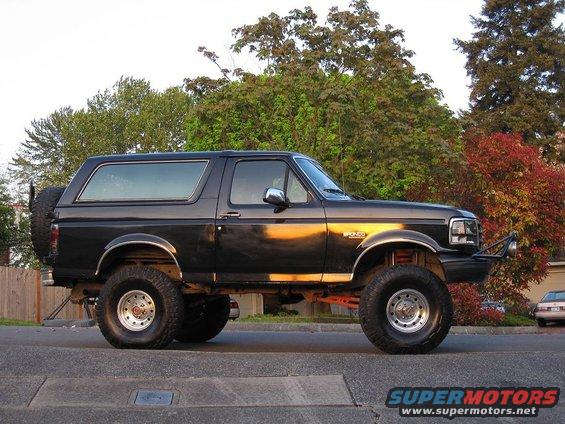 Black 1992 Ford Bronco, lifted, with spare tire on rear door, parked on street