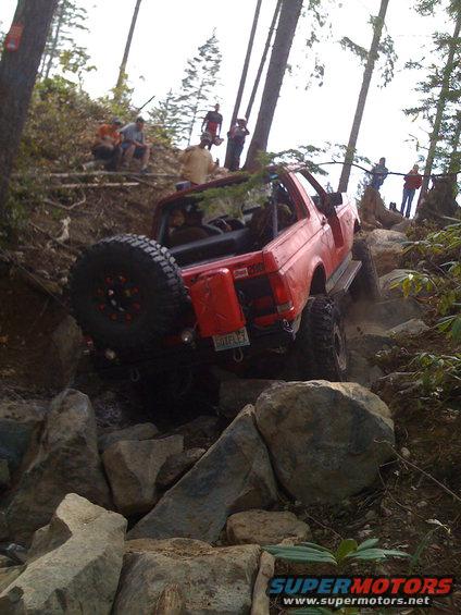 Red 1992 Ford Bronco on rocky trail, rear view with spare tire and gas can