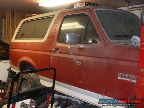 Red Ford Bronco parked inside a garage, side view shows the front door and rear quarter panel