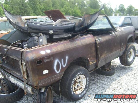 Brown International Scout II pickup truck with a black Dodge Ram bumper on top, in a junkyard