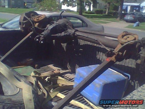 Pickup truck bed loaded with old vehicle parts, straps, and a blue cooler