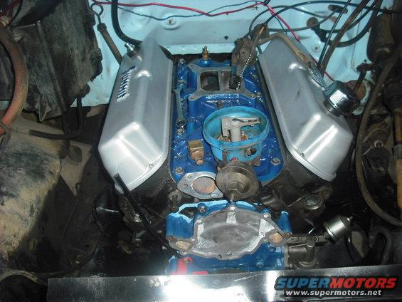 V8 engine with blue intake manifold, silver valve covers, and distributor. Supermotors.net logo visible
