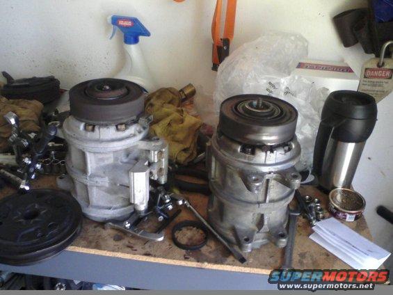 Two car AC compressors sit on a workbench with tools and a spray bottle