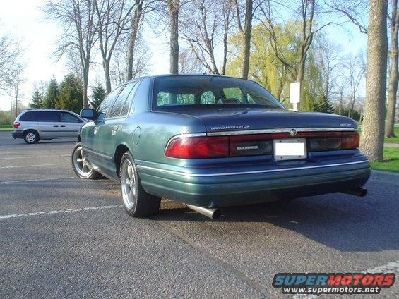 Green Mercury Grand Marquis, rear 3/4 view, showing custom wheels and dual exhaust