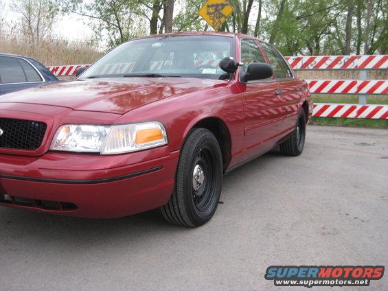 Red 2000 Ford Crown Victoria parked next to a blue car, with red and white striped barriers behind it