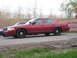 2000 Ford Crown Victoria - Two sedans are parked side-by-side on a dirt road, with a striped barrier in the background.