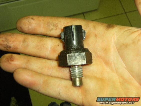 Hand holding a black automotive sensor with a hex nut base and threaded end