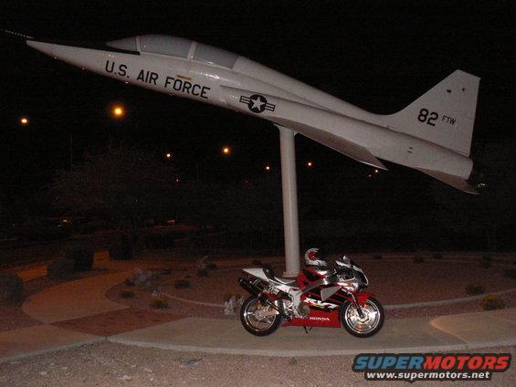 Red and white Honda motorcycle parked near a U.S. Air Force jet on display at night