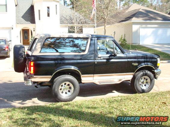 Black Ford Bronco with tan top and trim, spare tire on rear, parked on grass