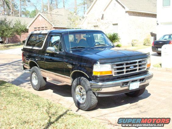 Black 1996 Ford Bronco parked in driveway, tan lower body trim, chrome wheels