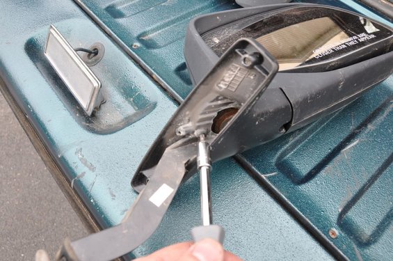 hand unscrewing a car mirror on a teal truck bed