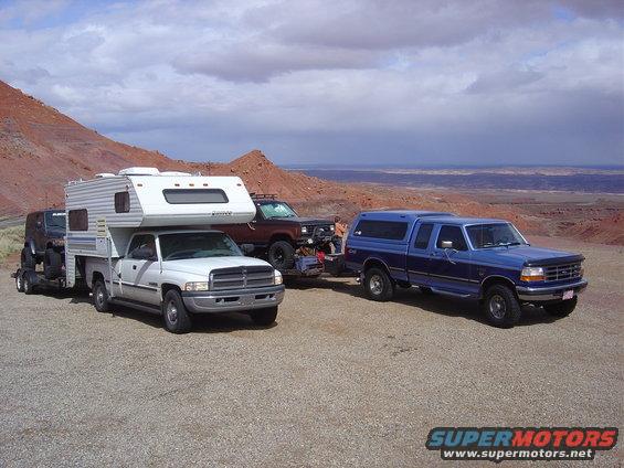 Three trucks and a trailer with a vehicle on it, parked in a desert landscape