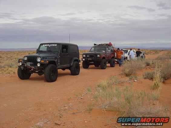 Several off-road vehicles parked on a dirt track in a desert landscape