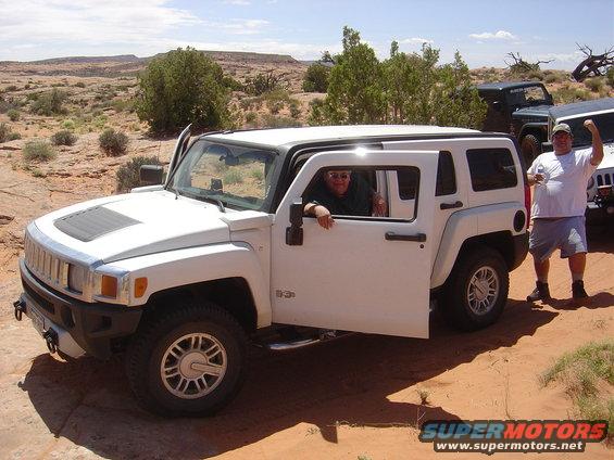 White Hummer H3 with open door, people inside and outside, in a desert landscape