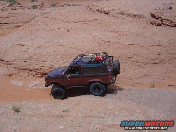 Brown 1986 Ford Bronco II with roof rack and spare tire driving on rocky terrain