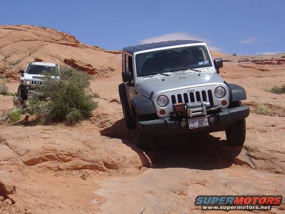 Silver Jeep Wrangler and white Hummer H3 driving on rocky desert terrain