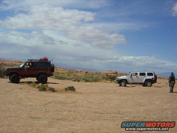 Red Ford Bronco II and white Hummer H3 parked on dirt terrain under a cloudy sky