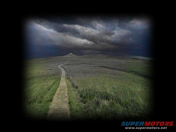 Dirt path winds through grassy hills under a stormy sky