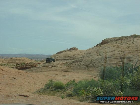 Off-road vehicle driving on a rocky, desert landscape under a cloudy sky