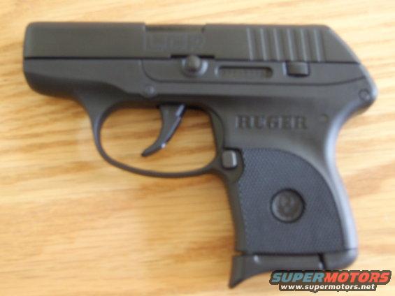 Black Ruger LCP pistol on wooden surface. Text on slide reads LCP and RUGER. Supermotors.net logo in corner
