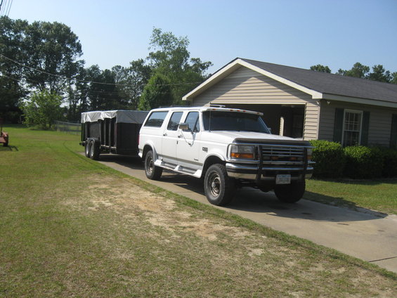 White Ford Bronco SUV towing a covered utility trailer in a driveway