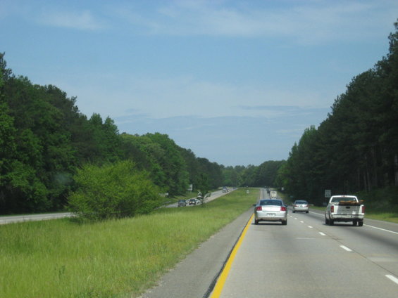 White pickup truck driving on a highway with trees lining the sides