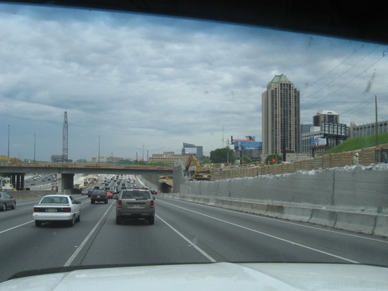 Driving on a highway with construction on the right and a tall building in the distance