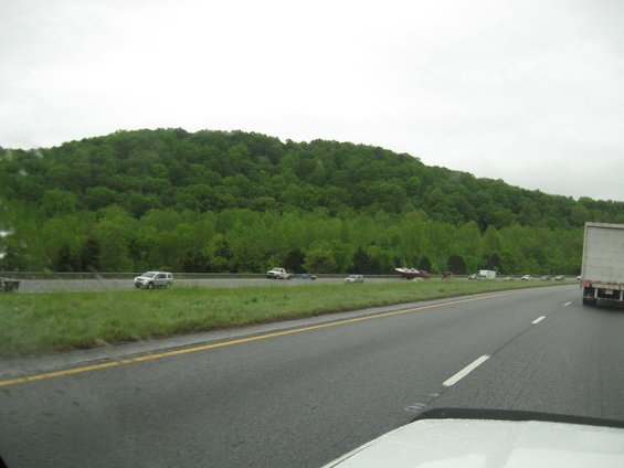 Highway scene with a white truck in the foreground and a wooded hill in the background