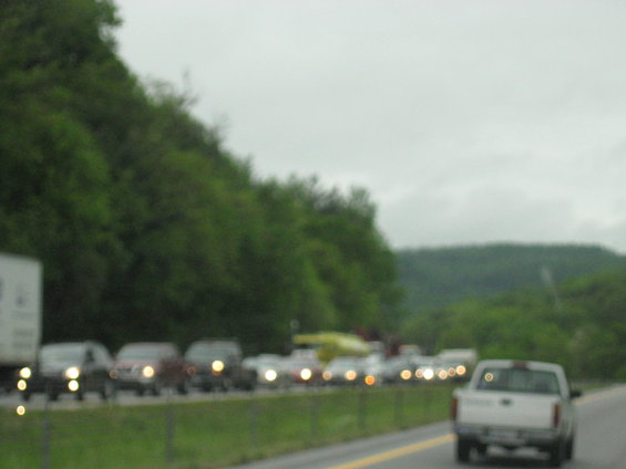 White pickup truck in foreground, traffic jam on highway with green trees and hills in background