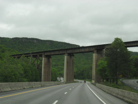 Railroad bridge with concrete pillars over a wet highway with green trees and mountains in the background