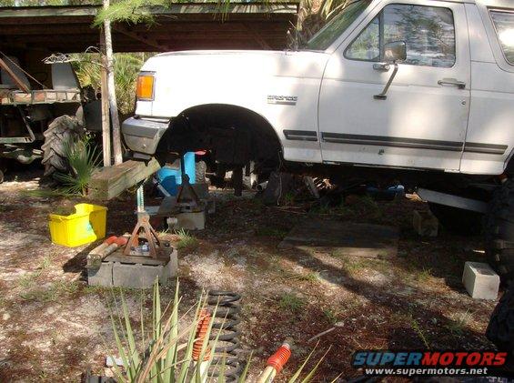 White Ford Bronco on jack stands, front wheel removed, under a covered area
