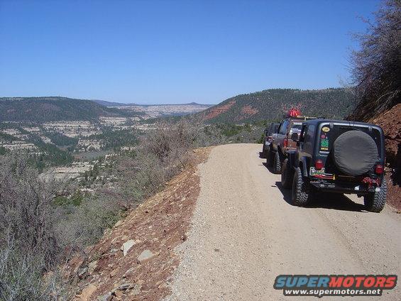 Four off-road vehicles parked on a dirt road overlooking a canyon