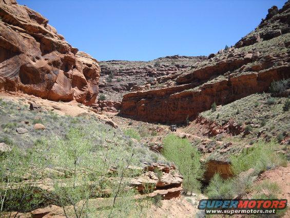 Off-road vehicle navigates a canyon path under a clear blue sky