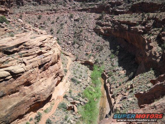 Dirt road winds through a rocky canyon with a dry creek bed and green trees
