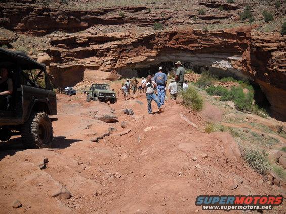 Green off-road vehicle on a rocky trail with people walking