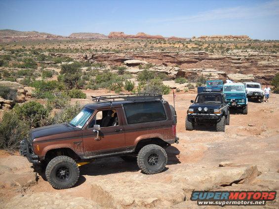 Brown Ford Bronco II with roof rack and off-road tires driving on rocky terrain
