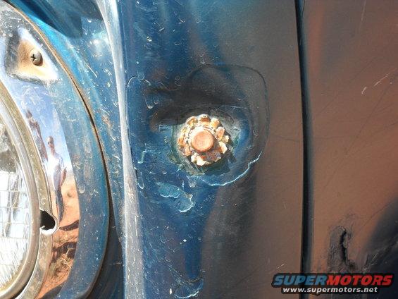 Blue vehicle fender detail with rusty bolt and headlight trim