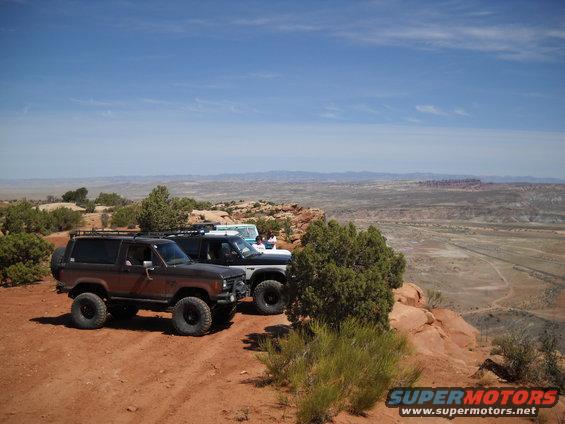 1986 Ford Bronco II and two other SUVs parked on a rocky overlook with a vast desert valley below