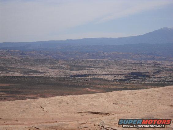 wide desert view with mountains in distance, rocky foreground, and a dirt road winding through the terrain