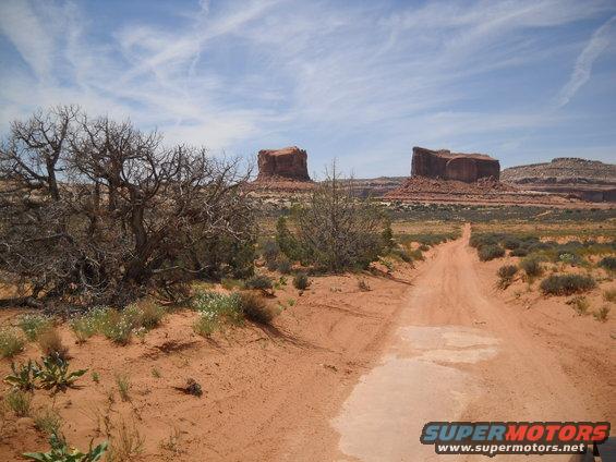 Dirt road leading through a desert landscape with mesas under a blue sky with clouds